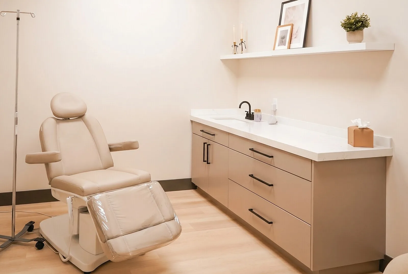 A treatment room at the spa: a made bed under warm light, cabinetry, and a laser arm folded back against the wall.