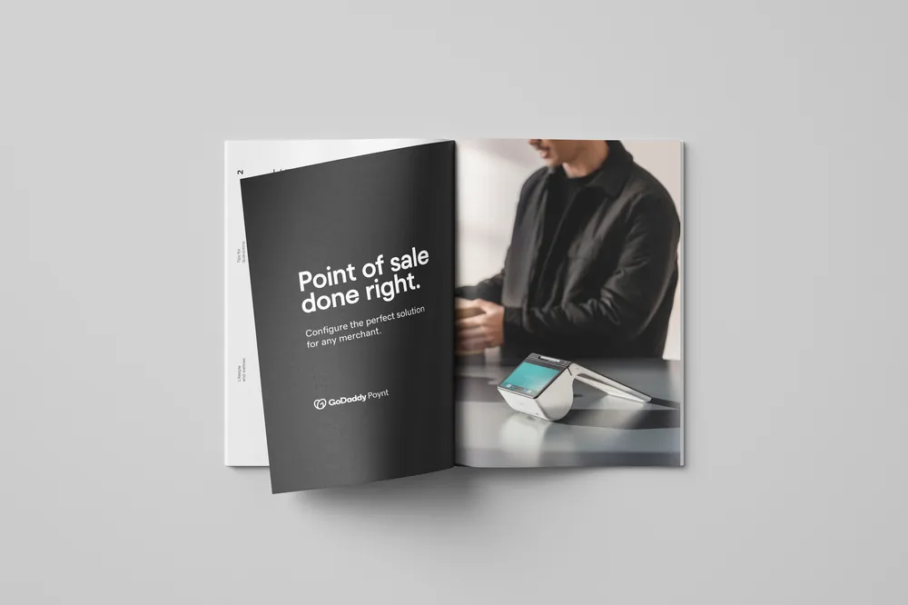 Open magazine spread: a black left page carrying the headline 'Point of sale done right.' and the GoDaddy Poynt lockup, facing a full-bleed photograph of a merchant at a counter with a white Poynt terminal.